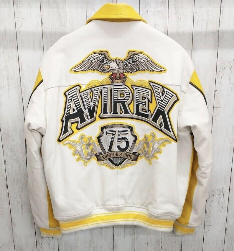 May include: White and yellow bomber jacket with the word "AVIREX" and an eagle emblem on the back. The jacket has yellow stripes on the sleeves and a yellow collar. The text "75 AVIATOR'S KING" is also visible.