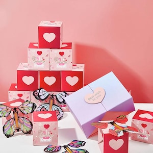 Pode incluir: Uma coleção de caixas de presente em vários tamanhos e designs, com motivos de coração e borboleta. As caixas são principalmente vermelhas e rosas, algumas exibem o texto "Surprise" e "Best wish to you". Brinquedos decorativos de borboleta também estão presentes.