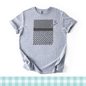 Puede incluir: Una camiseta de manga corta en color gris jaspeado con un estampado gráfico negro en el pecho. El diseño consta de tres secciones horizontales con un patrón de chevrón, rayas sólidas y un patrón de rejilla de diamantes, con pequeñas aves.