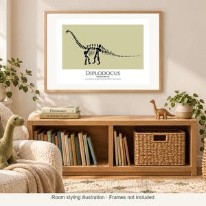 May include: A framed wall art print featuring a black silhouette of a Diplodocus dinosaur skeleton on a light olive green background. The text below the dinosaur reads DIPLODOCUS, followed by smaller descriptive text in a serif font.