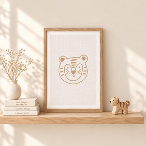 Pu&ograve; includere: Una stampa verticale incorniciata che presenta un'illustrazione a linee di un muso di tigre in marrone su uno sfondo beige testurizzato. La cornice &egrave; in legno chiaro. Accanto si trovano una piccola statuetta di tigre in legno e un vaso di fiori secchi.
