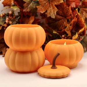 May include: Three orange pumpkin-shaped containers with ribbed textures. Two containers are stacked vertically, while the third sits beside them with its matching lid featuring a brown stem placed in front of the open pumpkin base.