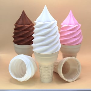 May include: Three soft-serve ice cream cone replicas in brown, white, and pink, each featuring a spiralled top and a textured waffle cone base. Two additional empty waffle cone bases are positioned in the foreground, showing a grid pattern.