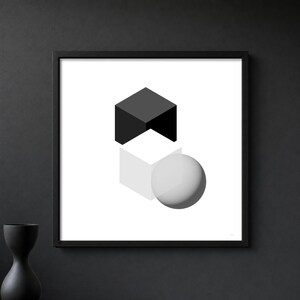May include: A framed square wall art print featuring a geometric composition of a solid black cube positioned above a translucent white cube, with a smooth grey sphere resting partially in front of the lower cube on a plain white background.