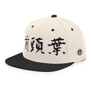 Könnte beinhalten: Cremefarbene Baseballkappe mit schwarzem Schirm. Die Kappe hat schwarze japanische Schriftzeichen auf der Vorderseite und ein kleines Logo an der Seite. Die Kappe hat einen flachen Schirm und einen Knopf oben.