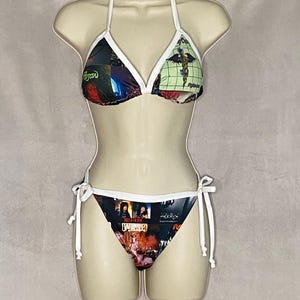 May include: A two-piece bikini set with a halter top and tie-side bottoms. The bikini features a collage of images and text in various colors, with white trim and ties. The top has a triangle shape, and the bottoms are a classic cut.