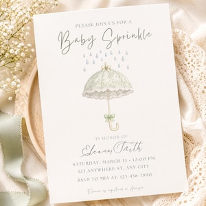 以下が含まれることがあります： ベビーシャワーの招待状、傘のイラスト付き。「PLEASE JOIN US FOR A Baby Sprinkle」のテキストとイベントの詳細が記載されています。傘はレース模様と緑のリボンが付いた淡い緑色です。