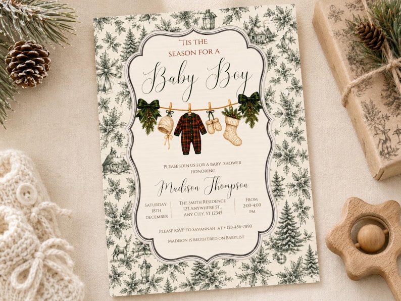 K&ouml;nnte beinhalten: Eine rechteckige Einladungskarte f&uuml;r eine Babyparty mit cremefarbenem Hintergrund und einem dunkelgr&uuml;nen botanischen Muster aus Tannen und Stechpalmen. Der Text lautet 'Tis the season for a baby boy' &uuml;ber einer W&auml;scheleine mit Babykleidung.