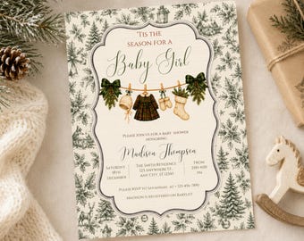 May include: A rectangular baby shower invitation card featuring a cream background with a dark green botanical border of pine trees and holly. The center displays a clothesline with a hat, dress, mittens, and stocking, with text reading 'Tis the season for a Baby Girl' and event details.