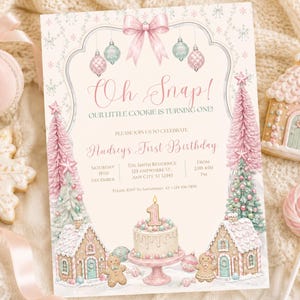 May include: A rectangular birthday invitation card featuring a pink bow, hanging ornaments, gingerbread houses, pink Christmas trees, and a cake with a number one candle. The text reads: Oh Snap! Our Little Cookie Is Turning One! Audrey's First Birthday.