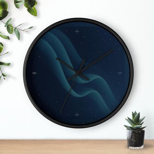 Pode incluir: Relógio de parede redondo com moldura preta. O mostrador apresenta um fundo azul escuro com formas turquesas fluidas e pequenos pontos brancos. Os ponteiros pretos indicam as horas. Uma pequena planta em vaso está em uma superfície de madeira.