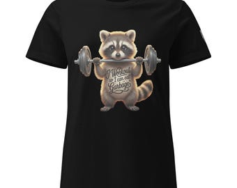 Peut inclure: T-shirt noir avec un raton laveur de dessin animé soulevant des poids. Le raton laveur a une expression déterminée et le texte "I Workout so I can eat Garbage" est imprimé sur le t-shirt. Le t-shirt est en matière souple.