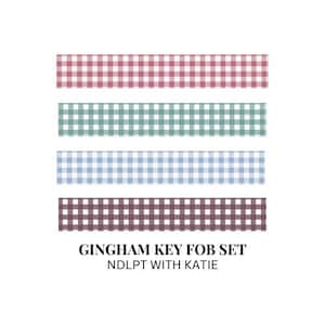 Peut inclure: Ensemble de quatre porte-clés rectangulaires à carreaux vichy rouges, verts, bleus et violets. Le texte "GINGHAM KEY FOB SET" et "NDLPT WITH KATIE" est affiché en dessous.