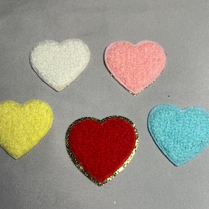 May include: Five heart-shaped patches in various colors: white, pink, yellow, red, and blue. Each patch has a textured, fuzzy surface. The red heart has a gold trim. These patches are suitable for crafts and embellishments.