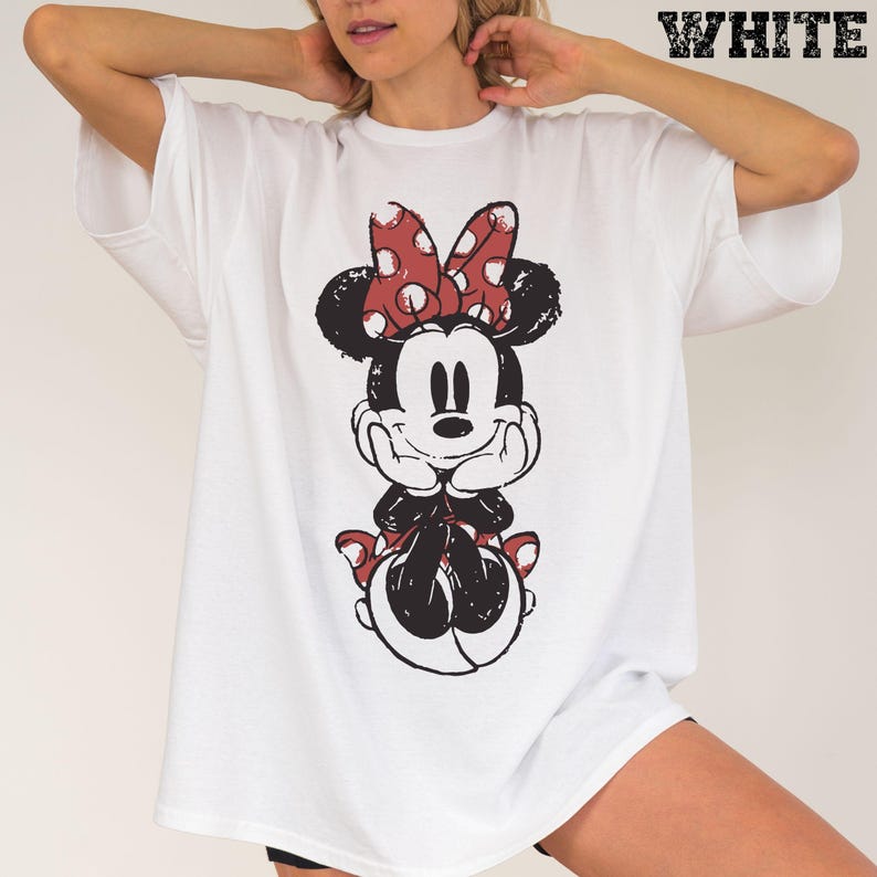 May include: White t-shirt featuring a distressed graphic of Minnie Mouse with a red polka dot bow. The word "WHITE" is printed in a bold, textured font at the top right corner. The shirt has short sleeves and a relaxed fit.