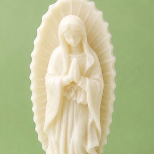 Può includere: Una candela in cera color bianco sporco modellata a forma di figura con le mani giunte in preghiera. La figura indossa una lunga veste ed è circondata da un'aureola smerlata a raggiera. Uno stoppino bianco sporge dalla sommità del capo.