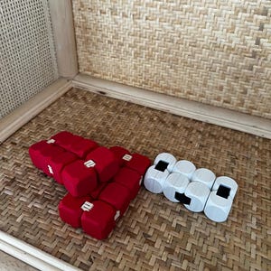 Può includere: Due set di giocattoli modulari geometrici. Un set è composto da cubi rossi con connettori bianchi, disposti in un gruppo. L'altro set è bianco con inserti neri, anch'essi in un gruppo. I giocattoli sono su una superficie tessuta.