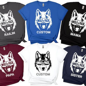 May include: A collection of t-shirts in various colors, each featuring a wolf graphic wearing sunglasses. The text "WOLF PACK" is above the wolf's face. Some shirts have additional text like "RAILIN", "CUSTOM", "MAMA", "PAPA", and "SISTER".