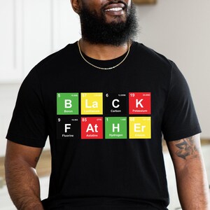 May include: Black t-shirt with a periodic table design spelling out "BLACK FATHER". The design features the elements Boron, Carbon, Potassium, Fluorine, Astatine, Hydrogen, and Erbium in colorful squares. The shirt is short-sleeved.