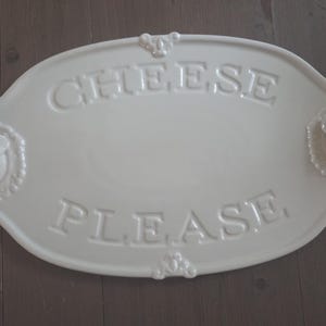 May include: Off-white oval cheese serving platter with embossed text reading "CHEESE PLEASE". The platter features decorative mouse head accents on each end. A charming addition to any kitchen.