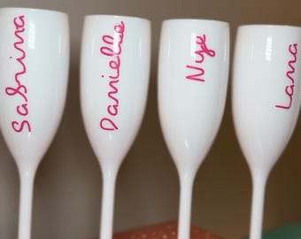 Può includere: Quattro flute di champagne bianche con nomi scritti in rosa: Sabrina, Danielle, Nye e Lama. Le flute sono disposte su una superficie rosa glitterata, ideali per una festa.