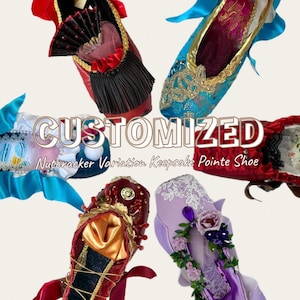 May include: Five decorative pointe shoes arranged in a circle, each featuring unique embellishments like lace, ribbons, beads, and floral accents. The text CUSTOMIZED Nutcracker Variation Keepsake Pointe Shoe is centered in the middle of the display.