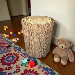 May include: A beige tree stump side table with a textured bark-like exterior and a light brown top. A brown teddy bear sits next to the table. Colorful toy blocks and a patterned rug are in the foreground.