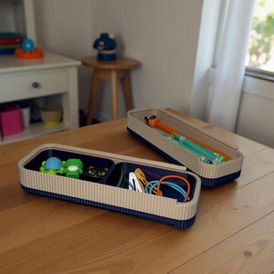 May include: Two rectangular storage containers with a beige ribbed exterior and a navy blue base. One container holds toys, the other holds crayons and a marker. The containers are on a wooden table.