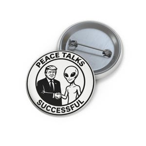 May include: A white button with the text "PEACE TALKS SUCCESSFUL" encircling an image of a handshake between a suited man and an alien. A second, similar button is partially visible in the background.