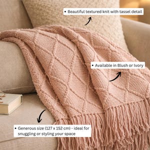 May include: A blush pink knit throw blanket featuring a diamond pattern and fringe trim. The blanket measures 127 cm by 152 cm. The text on the image includes: Beautiful textured knit with tassel detail, Available in Blush or Ivory, and Generous size (127 x 152 cm) - ideal for snuggling or styling your space.