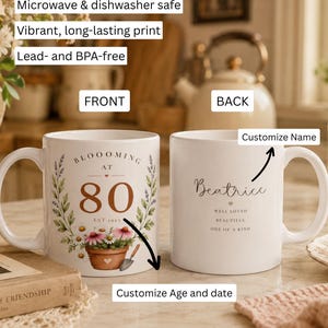 May include: Two white ceramic mugs featuring floral designs. The front mug displays the text BLOOOMING AT 80 EST. 1945 with a potted flower graphic. The back mug shows the name Beatrice with the text WELL LOVED, BEAUTIFUL, ONE OF A KIND.