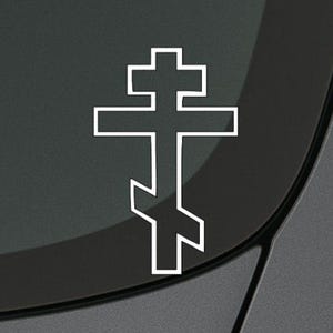 May include: White outline of a Russian Orthodox cross on a gray car window.