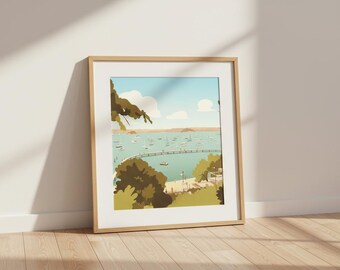 May include: A framed art print depicting a coastal landscape with a bridge, boats, and trees. The artwork features a color palette of blues, greens, and browns. The frame is a light wood color, and the print is leaning against a white wall on a wooden floor.