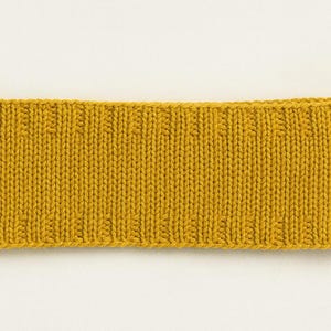 May include: Mustard yellow knitted headband. The headband is rectangular and features a ribbed knit pattern. The material appears to be soft and warm, suitable for cold weather. The background is plain white.