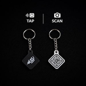 May include: Two square keychains with metal rings and chains. One black keychain features a white tattoo machine icon labeled TAP. The other white keychain displays a black QR code labeled SCAN. Both items are presented against a dark background.