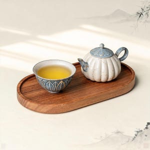 May include: A ceramic tea set with a blue and white teapot and a matching teacup filled with tea, resting on a wooden oval tray. The tea set has a floral design. The tray is made of wood.