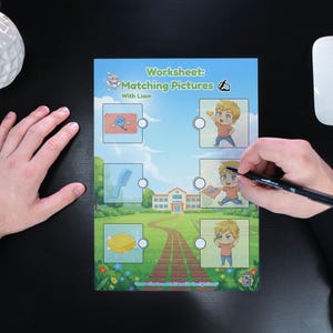 May include: A worksheet titled "Matching Pictures" with illustrations and the name "Liam". The worksheet is being completed with a black pen. A white mouse and a white vase with flowers are also visible.