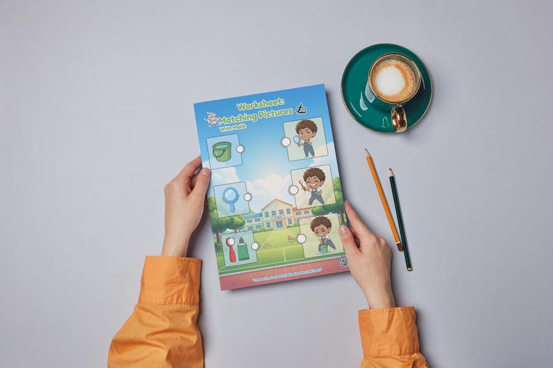 May include: A worksheet titled "Matching Pictures" with illustrations of objects and children. The worksheet is held by hands wearing an orange shirt. A cup of coffee and pencils are on the gray surface.