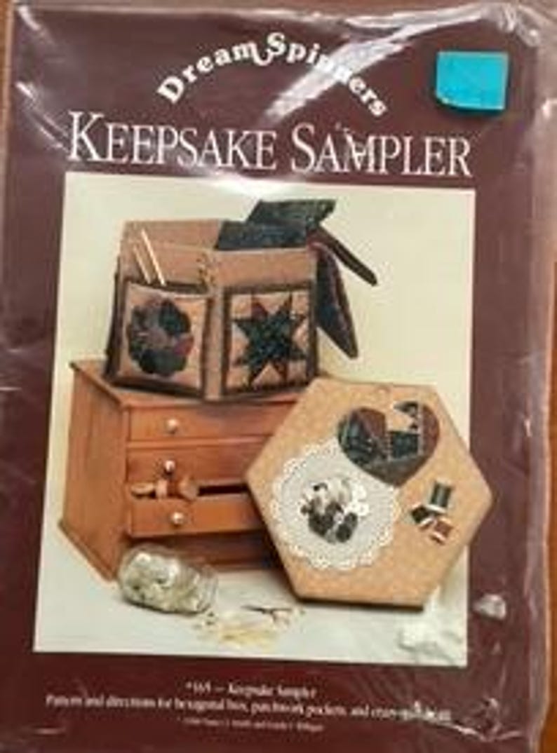 May include: A Keepsake Sampler kit by Dream Spinners. The image shows a wooden chest, a hexagonal box with a heart design, and a brown fabric bag with pockets. The kit includes patterns and directions for the items.