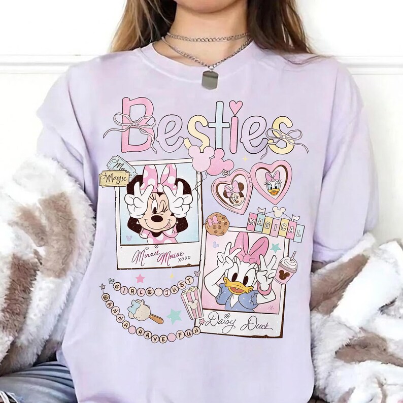 Peut inclure: Un sweat-shirt lilas clair avec le mot "Besties" dans une police fantaisie. Le motif comprend des images de Minnie Mouse et Daisy Duck, avec les mots "Magic" et "Magical". Le sweat-shirt a une coupe ample.