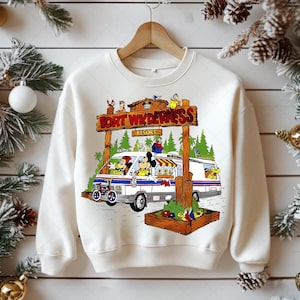 K&ouml;nnte beinhalten: Cremefarbenes Sweatshirt mit einem Aufdruck eines wei&szlig;en Vans mit Micky Maus und Freunden, beschriftet mit "Fort Wilderness Resort". Das Design umfasst ein Holzschild, B&auml;ume und Zeichentrickfiguren.