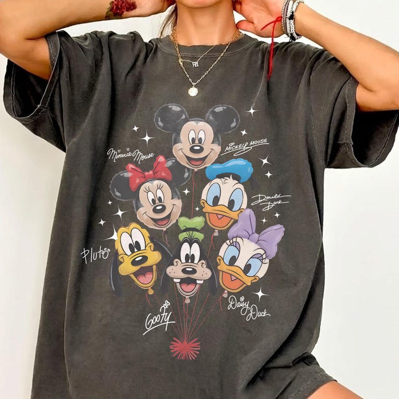 May include: Dark gray t-shirt featuring a graphic of Mickey Mouse and friends as balloons. The design includes Minnie Mouse, Donald Duck, Daisy Duck, Pluto, and Goofy. The names of the characters are written in script. The shirt has a vintage, distressed look.