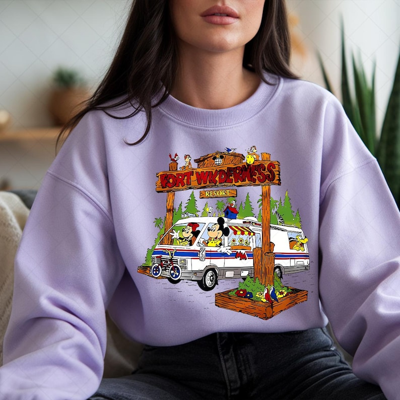 K&ouml;nnte beinhalten: Helllila Sweatshirt mit farbenfrohem Grafikdesign. Es zeigt einen wei&szlig;en und blauen Van mit Mickey und Minnie Mouse und anderen Figuren vor einem Holzschild mit der Aufschrift "Fort Wilderness Resort".