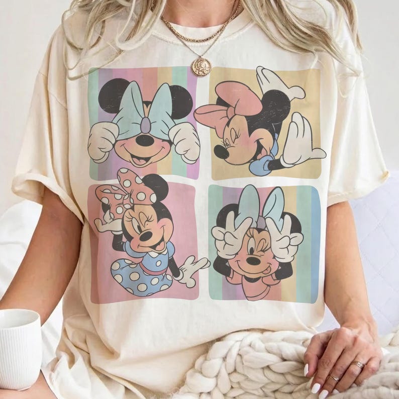 May include: Cream-colored t-shirt featuring a colorful Minnie Mouse graphic. The graphic is divided into four squares, each showcasing a different pose of Minnie Mouse with pastel backgrounds. The shirt has short sleeves and a relaxed fit.