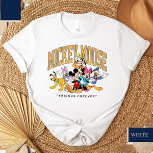 May include: White crew neck t-shirt with a graphic of Mickey Mouse and friends, including Donald Duck, Goofy, and Minnie Mouse. The text "MICKEY MOUSE" is arched above the characters, with "FRIENDS FOREVER" below.