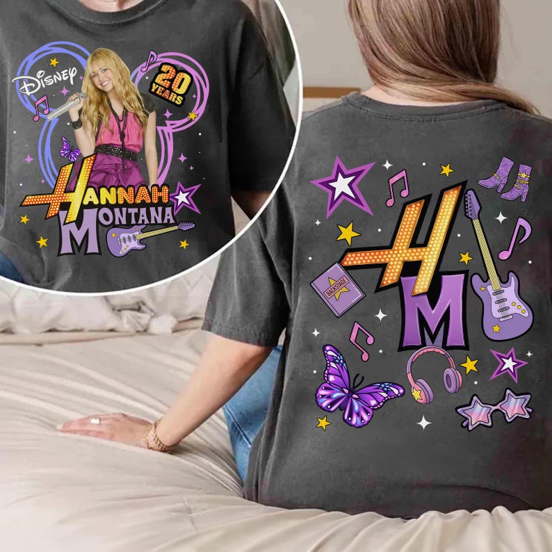 May include: Dark gray t-shirt featuring a graphic of Hannah Montana with the text "Hannah Montana" and "20 Years". The back of the shirt has musical notes, stars, and a guitar.