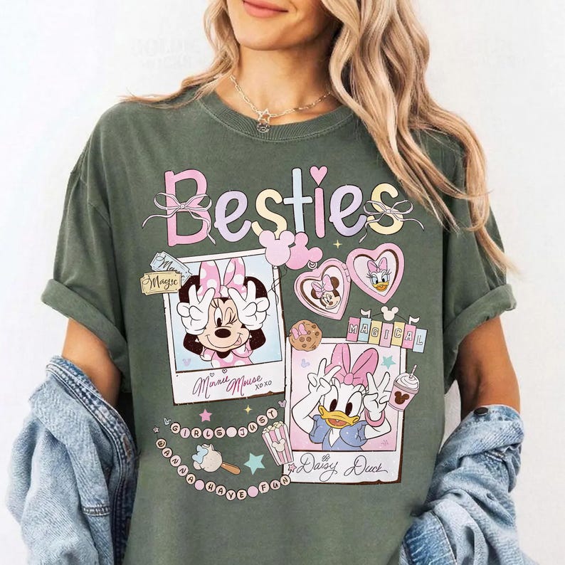 Peut inclure: T-shirt vert olive avec Minnie et Daisy Duck. Le t-shirt affiche le mot "Besties" en rose et bleu clair, ainsi que des images de dessins anim&eacute;s des personnages dans des cadres photo. Le design comprend des c&oelig;urs, des &eacute;toiles et les mots "Magical" et "XOXO".