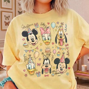 May include: Yellow t-shirt featuring Mickey Mouse, Daisy Duck, Pluto, Donald Duck, Goofy, and Minnie Mouse in party hats. The design includes cupcakes, balloons, and the text "Mickey Mouse", "Daisy Duck", "Donald Duck", and "Minnie Mouse xoxo".