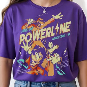 May include: Purple t-shirt featuring a graphic of cartoon characters with the text "POWERLINE WORLD TOUR '95". The design includes the phrases "STAND OUT" and "TILL MINE IS THE ONLY FACE YOU SEE."