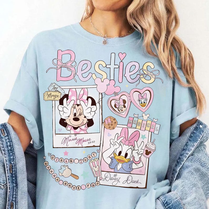 Peut inclure: T-shirt bleu clair avec le mot "Besties" en rose avec un n&oelig;ud. Le t-shirt pr&eacute;sente des graphiques de Minnie Mouse et Daisy Duck dans des cadres polaro&iuml;d, avec le texte "Minnie Mouse xoxo" et "Daisy Duck". D'autres graphiques sont &eacute;galement pr&eacute;sents.